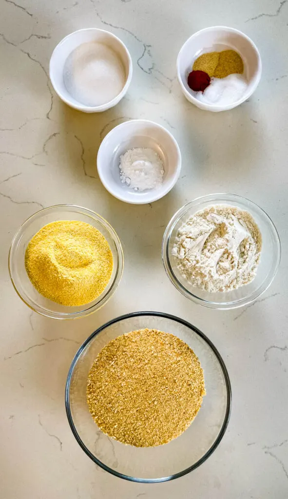 cornmeal, flour, baking powder, seasonings, and sweetener in separate bowls on a flat surface
