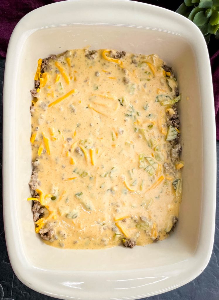 cooked ground beef in a casserole dish topped with shredded cheddar cheese