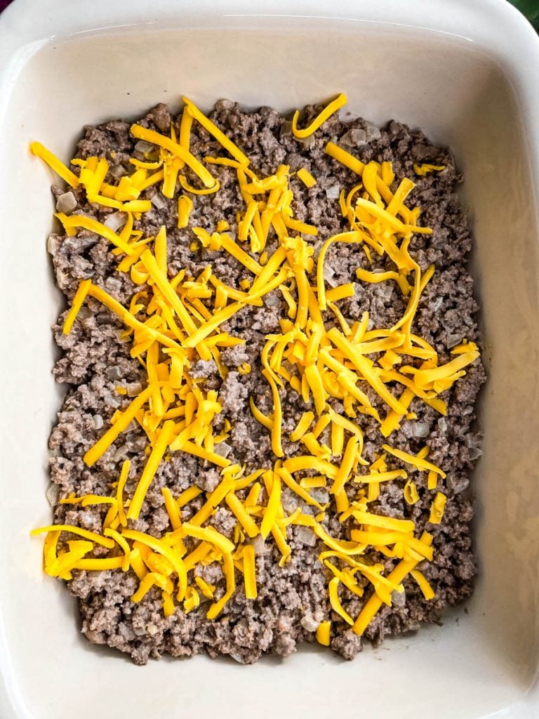 cooked ground beef in a casserole dish topped with shredded cheddar cheese