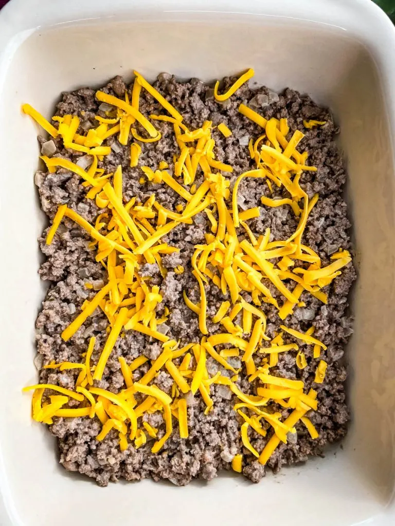 cooked ground beef in a casserole dish topped with shredded cheddar cheese