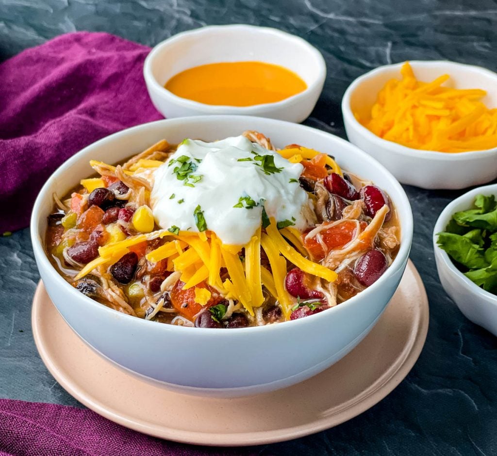 buffalo chicken chili in a white bowl with shredded cheese and sour cream