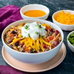 buffalo chicken chili in a white bowl with shredded cheese and sour cream