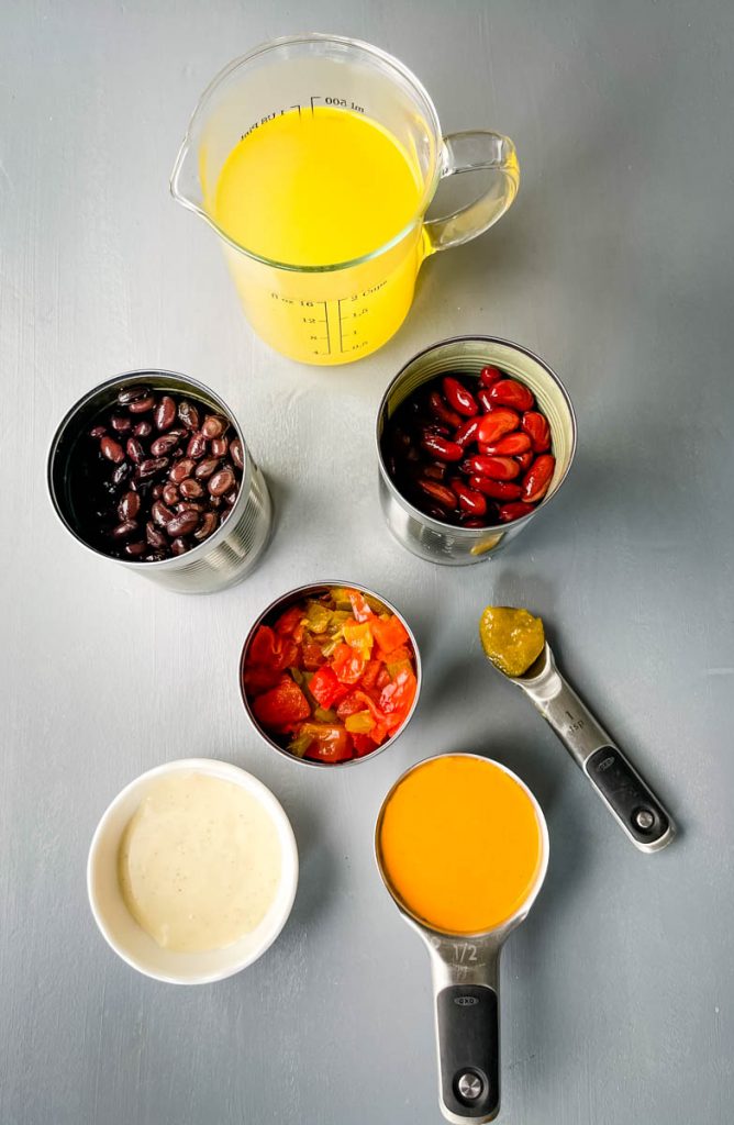 chicken broth, canned red beans, canned black beans, diced tomates, ranch, and buffalo sauce in separate containers on a flat surface