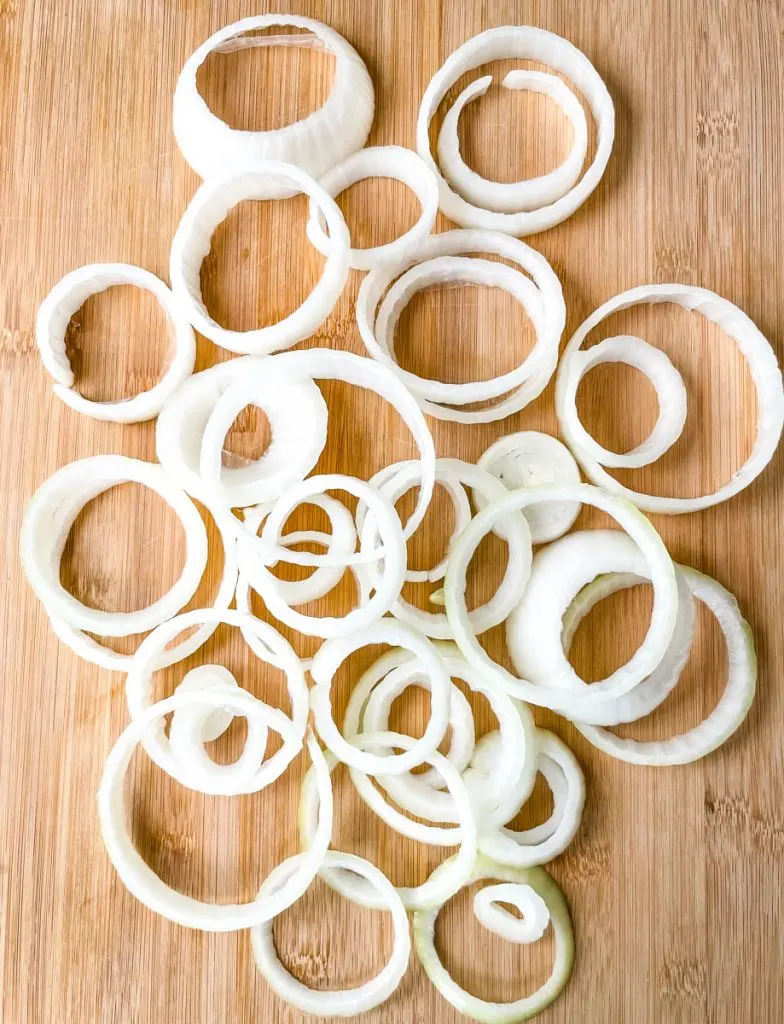 raw onions sliced into circles on a bamboo cutting board
