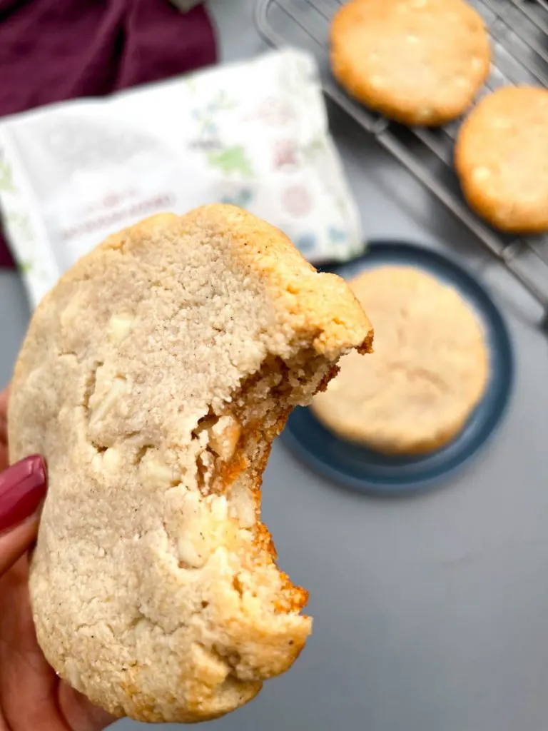 person holding keto macadamia nut cookie with a bite taken out