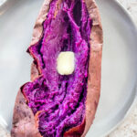 Stokes purple sweet potato fully cooked and sliced open on a plate with buter