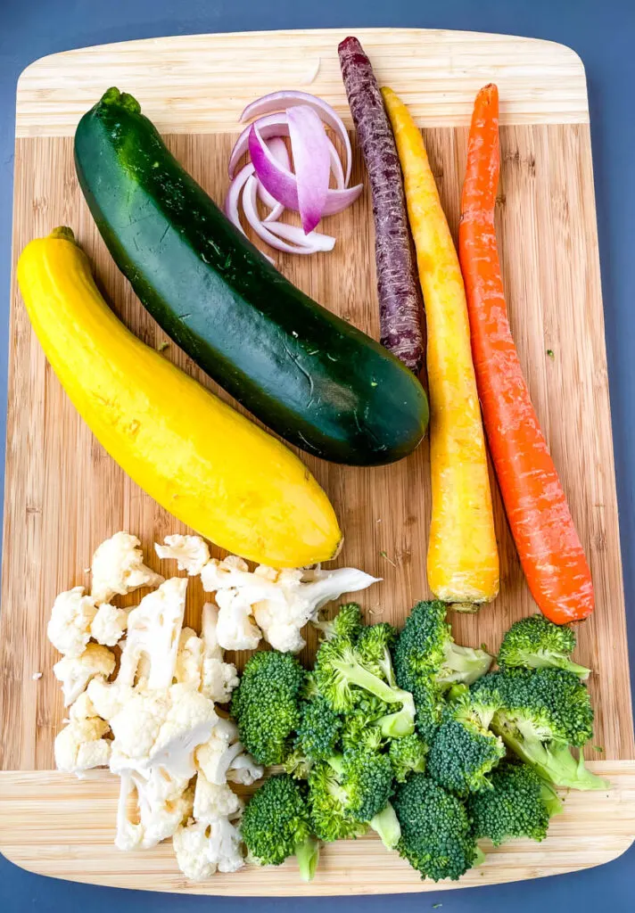squash, zucchini, onions, carrots, broccoli, and cauliflower on a bamboo cutting board