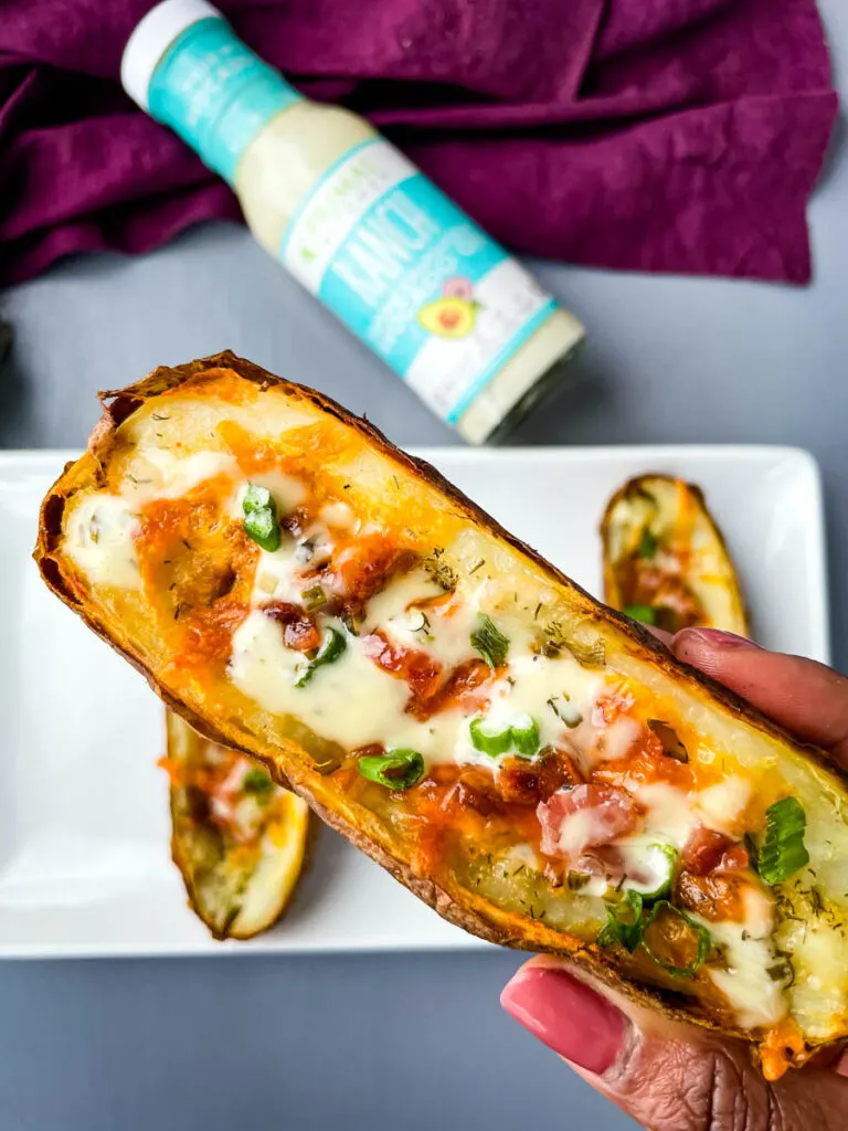 person holding air fryer potato skin drizzled in ranch