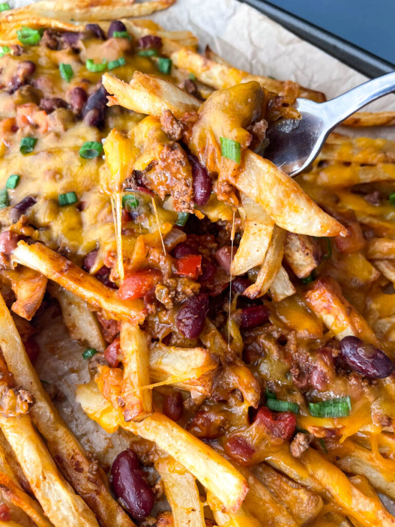 a fork full of chili cheese fries on a sheet pan