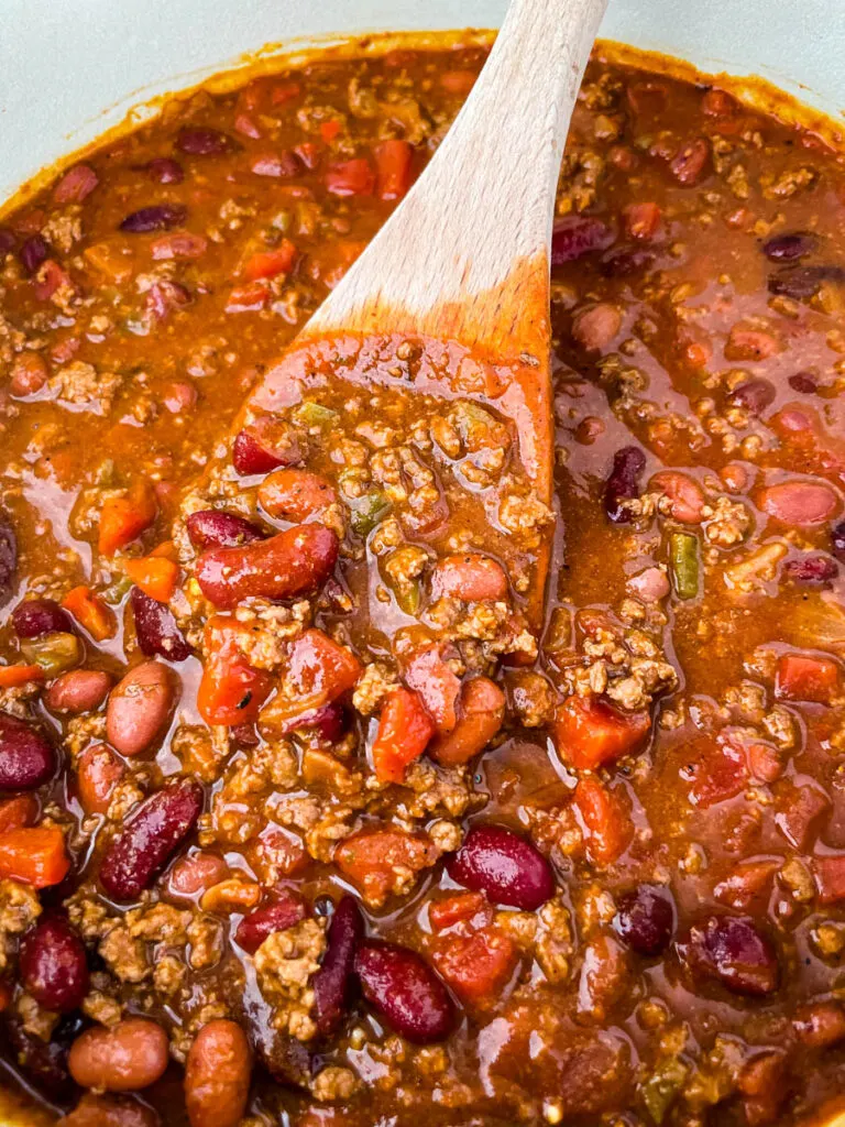 a wooden spoonful of beef chili in a Dutch oven