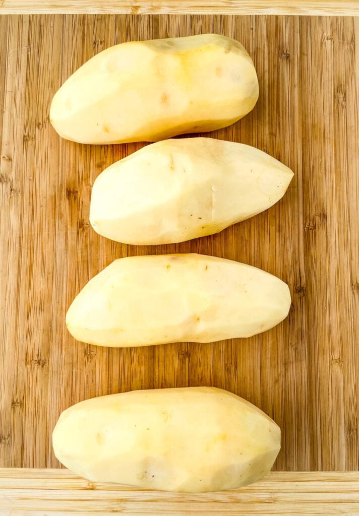 raw russet potatoes peeled on a bamboo cutting board