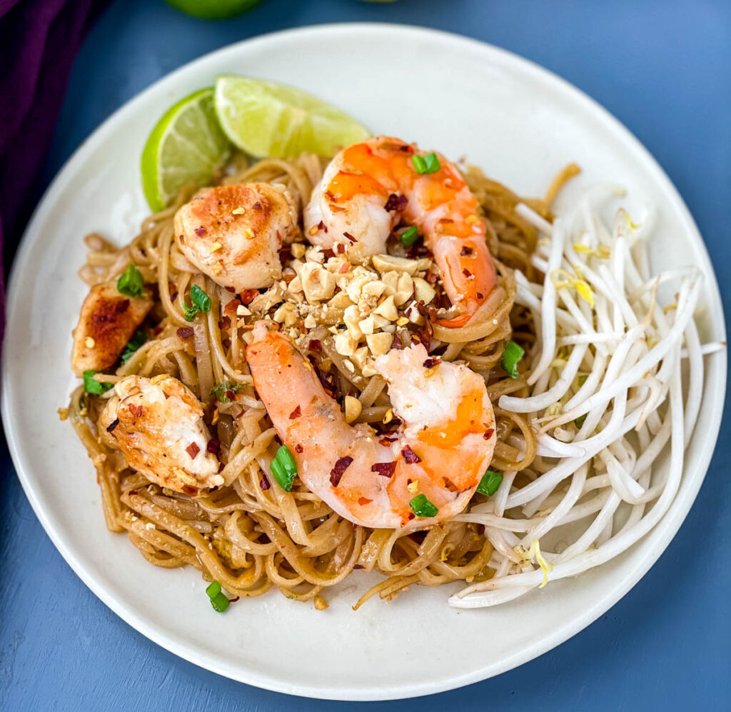 healthy pad thai with chicken, shrimp, bean sprouts, and lime on a white plate