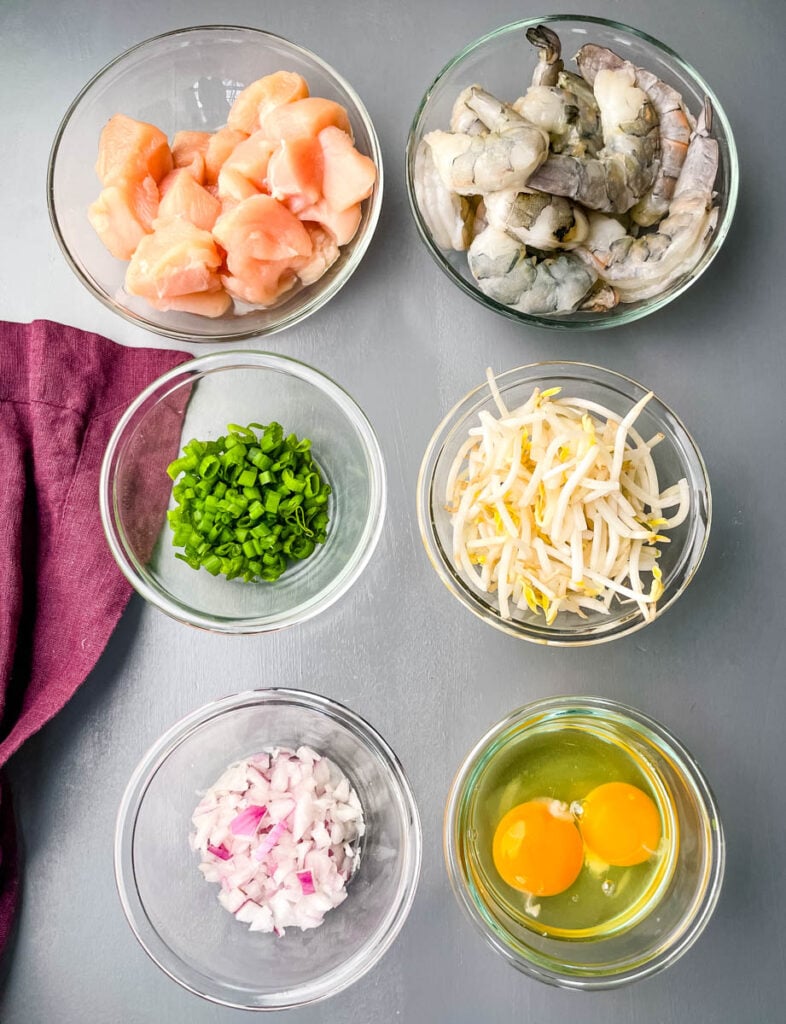 raw chicken, raw shrimp, chopped green onions, bean sprouts, chopped onions, and raw eggs in separate glass bowls