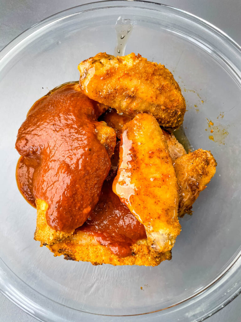 keto chicken wings in a glass bowl with maple syrup and BBQ sauce