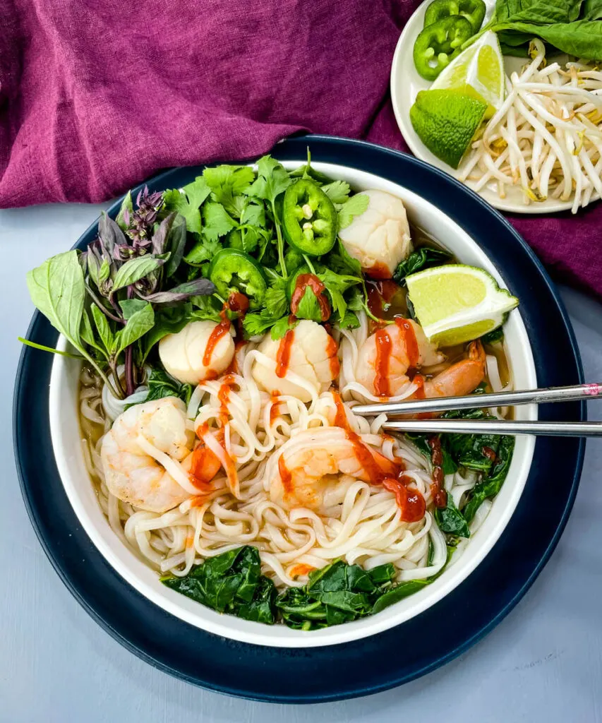 seafood shrimp pho in a white bowl drizzled with Sriracha