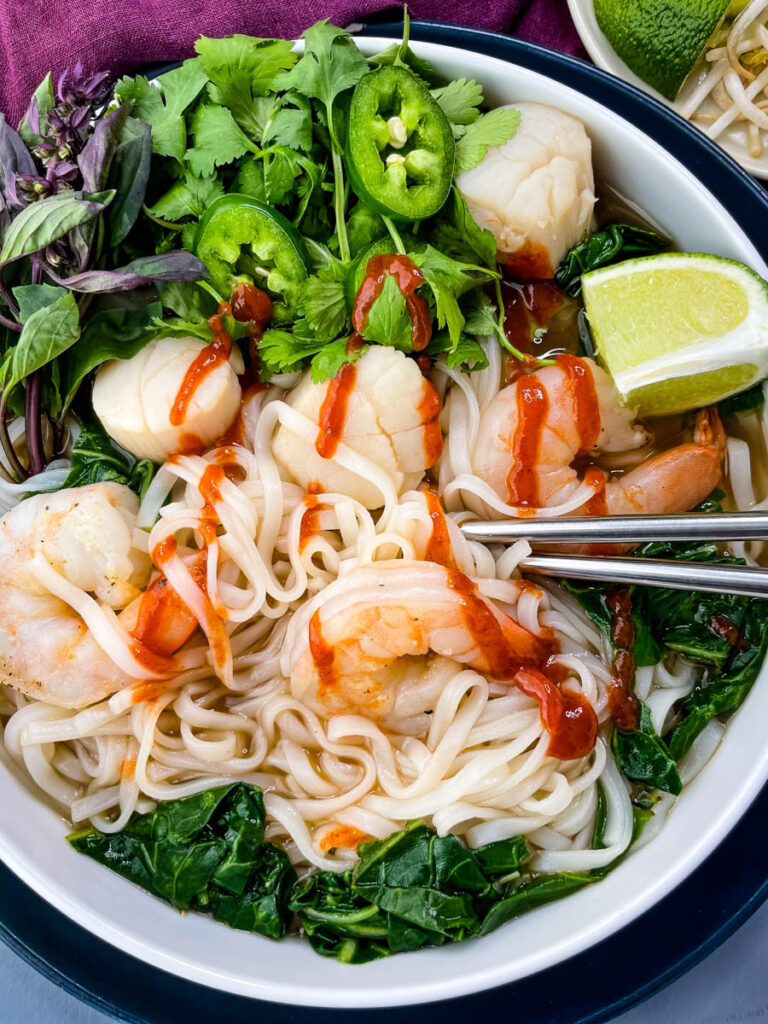 seafood shrimp pho in a white bowl drizzled with Sriracha