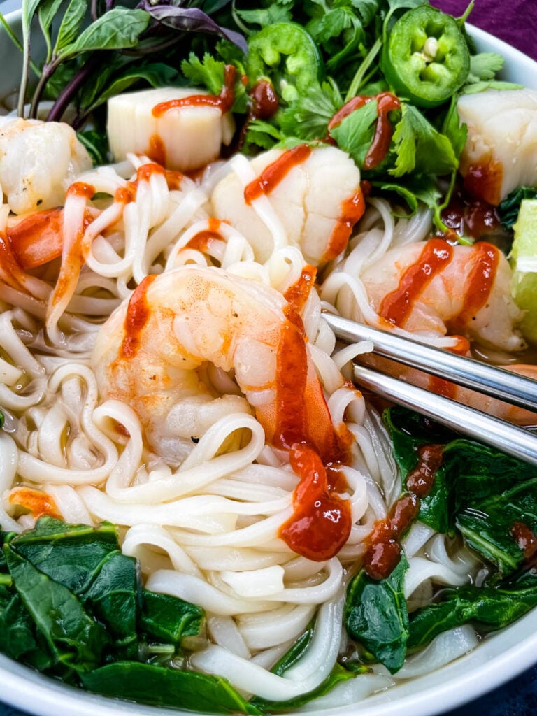 seafood shrimp pho in a white bowl drizzled with Sriracha