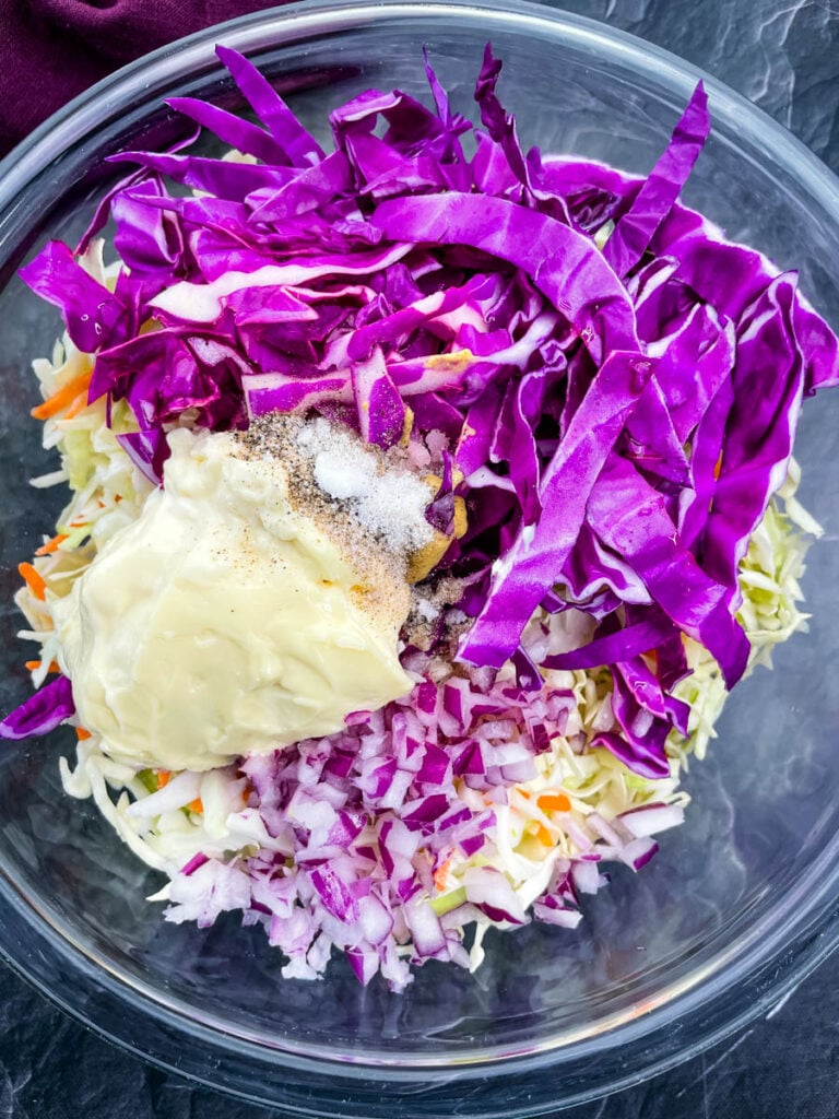 chopped red cabbage, coleslaw mix, chopped onions, mayo, and seasoning in a glass bowl