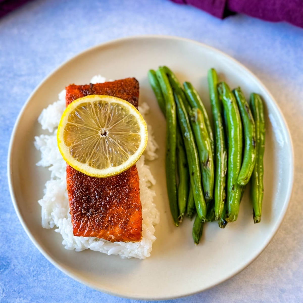 Air fryer salmon fillet served over white rice with green beans and a fresh lemon slice.
