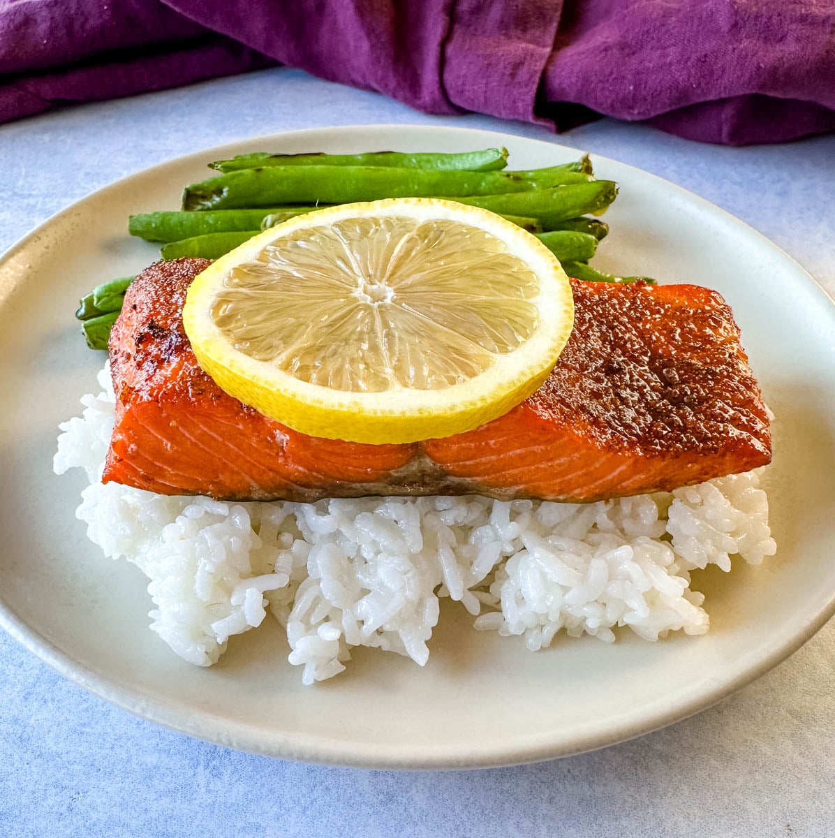 Air fryer salmon fillet served over white rice with green beans and a fresh lemon slice.