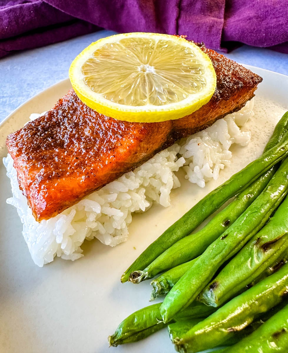 Close-up of seasoned air fryer salmon served over white rice with roasted green beans and lemon.