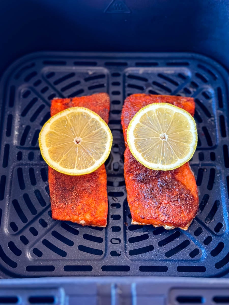 Two cooked salmon fillets topped with lemon slices inside an air fryer basket.