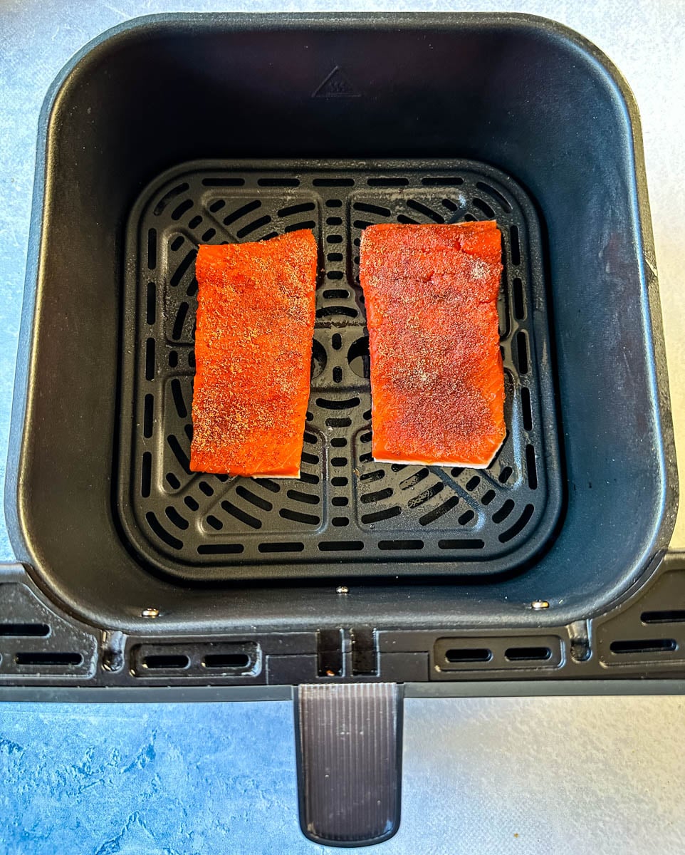 Two seasoned raw salmon fillets arranged in a single layer in an air fryer basket.