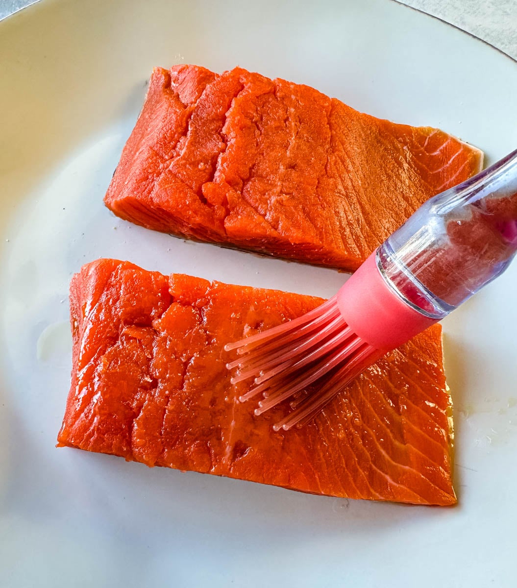 Raw salmon fillets being brushed with oil before seasoning and air frying.
