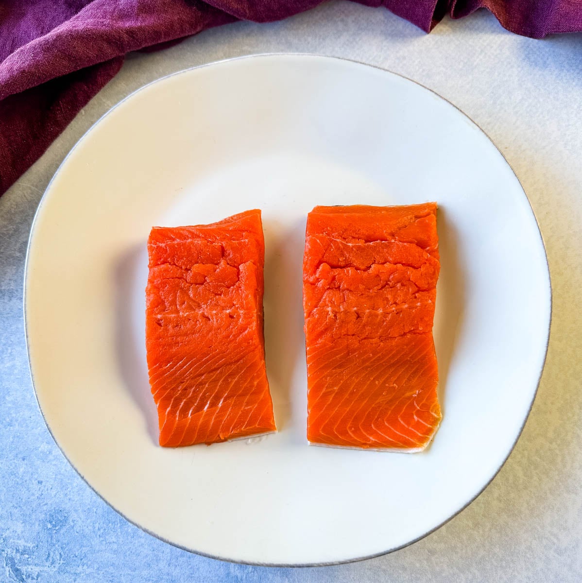 Two raw salmon fillets on a white plate before being oiled, seasoned, and air fried.