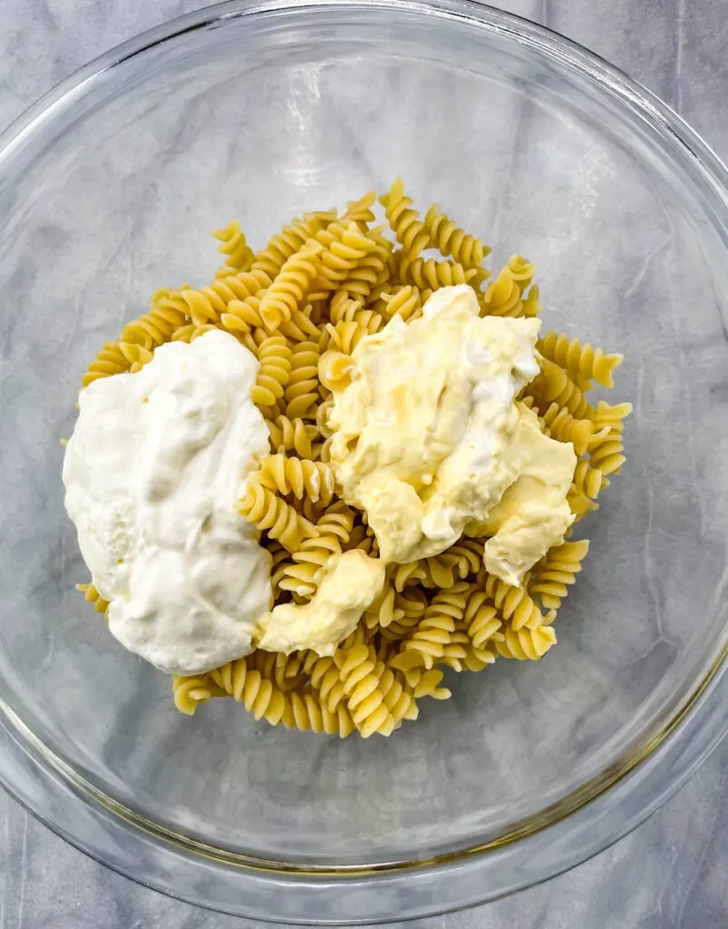 cooked rotini pasta in a glass bowl with mayo and greek yogurt