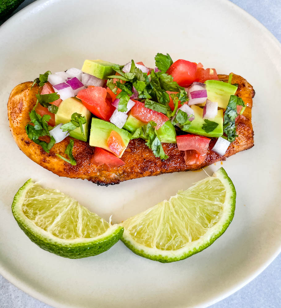 cooked chicken and avocado salsa on a plate with limes