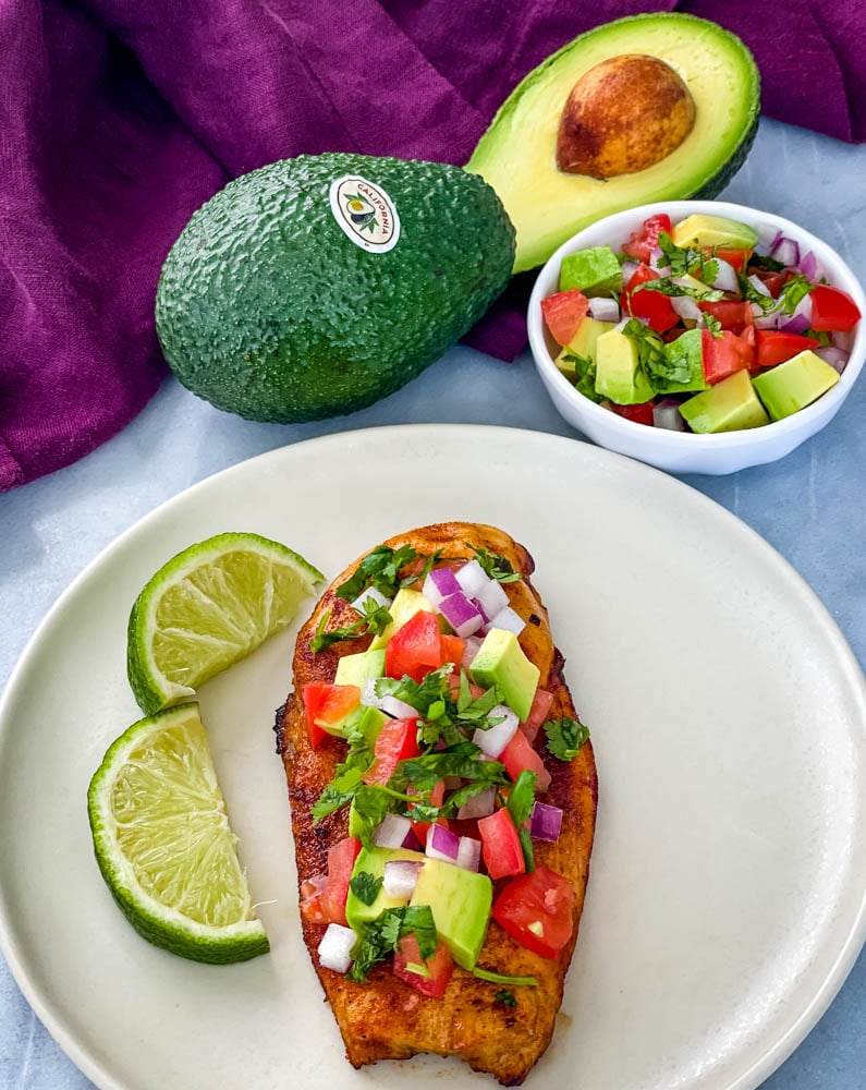 cooked chicken and avocado salsa on a plate with limes