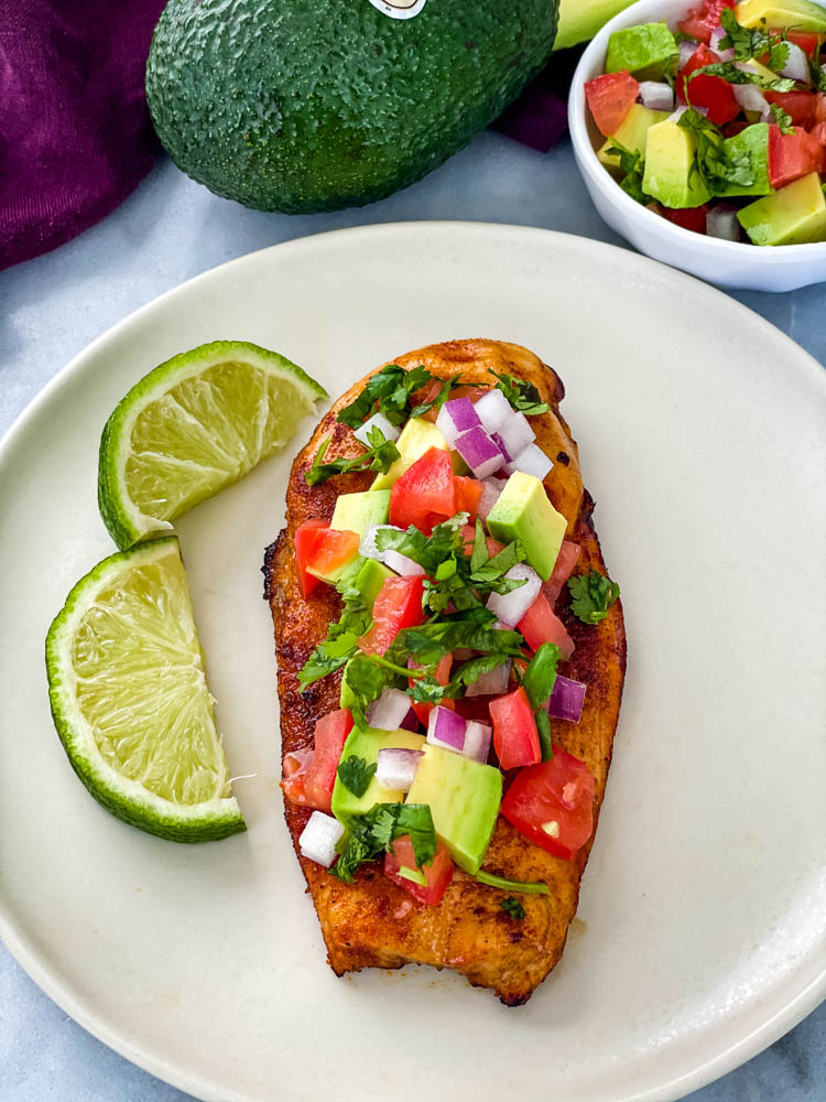 cooked chicken and avocado salsa on a plate with limes