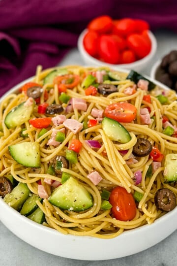 spaghetti salad in a white bowl with tomatoes and olivess