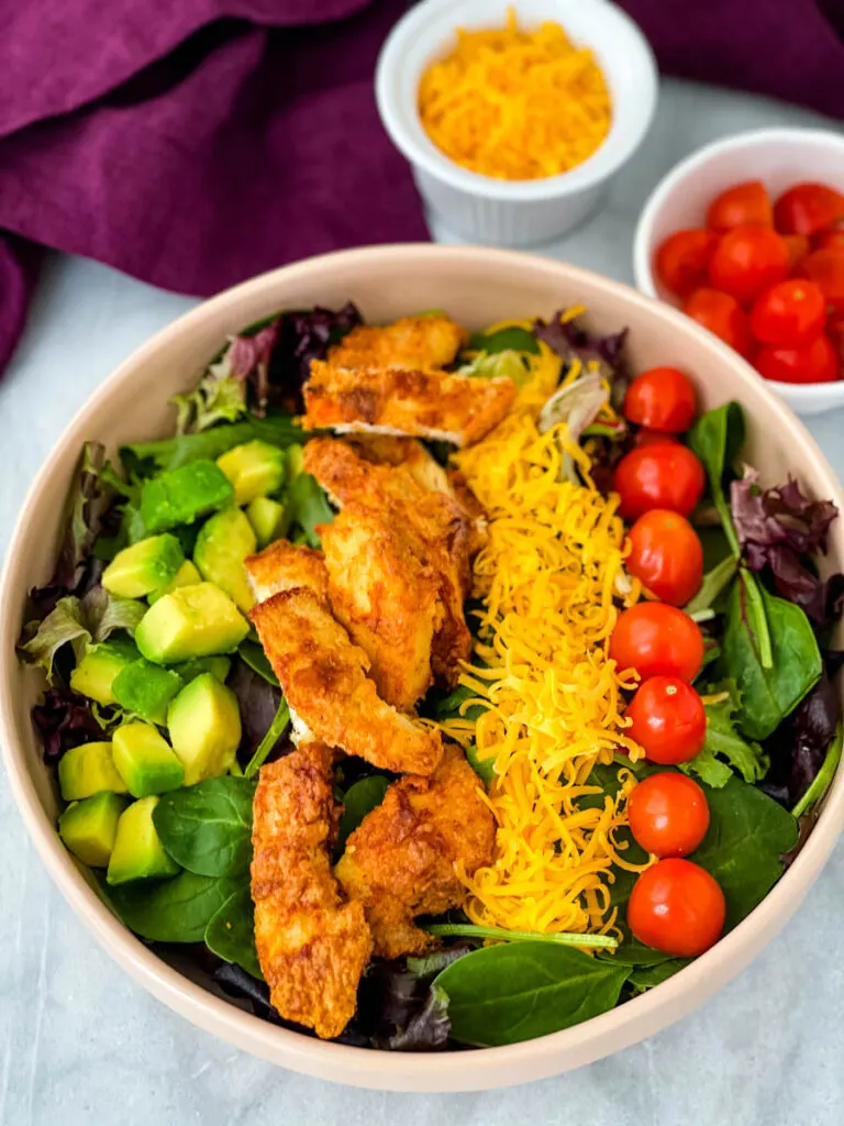 fried chicken salad in a pink bowl with avocado, tomatoes, and cheese