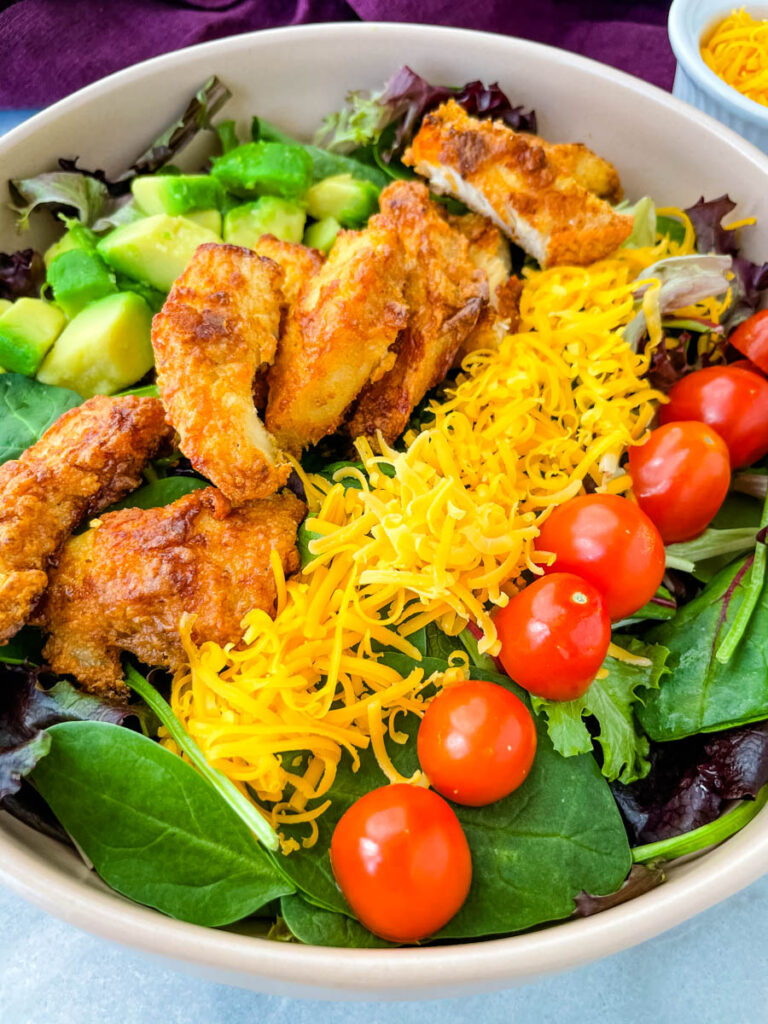 fried chicken salad in a pink bowl with avocado, tomatoes, and cheese