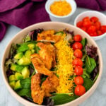 fried chicken salad in a pink bowl with avocado, tomatoes, and cheese