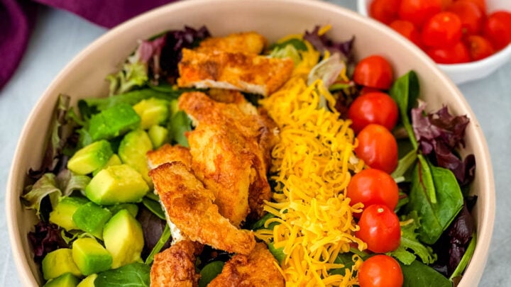 fried chicken salad in a pink bowl with avocado, tomatoes, and cheese