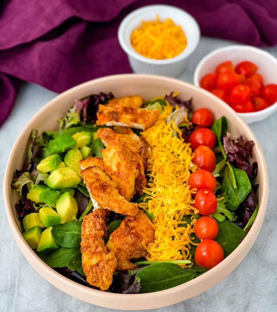 fried chicken salad in a pink bowl with avocado, tomatoes, and cheese