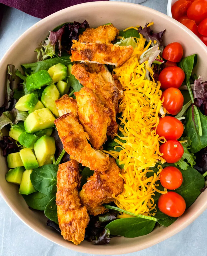 fried chicken salad in a pink bowl with avocado, tomatoes, and cheese