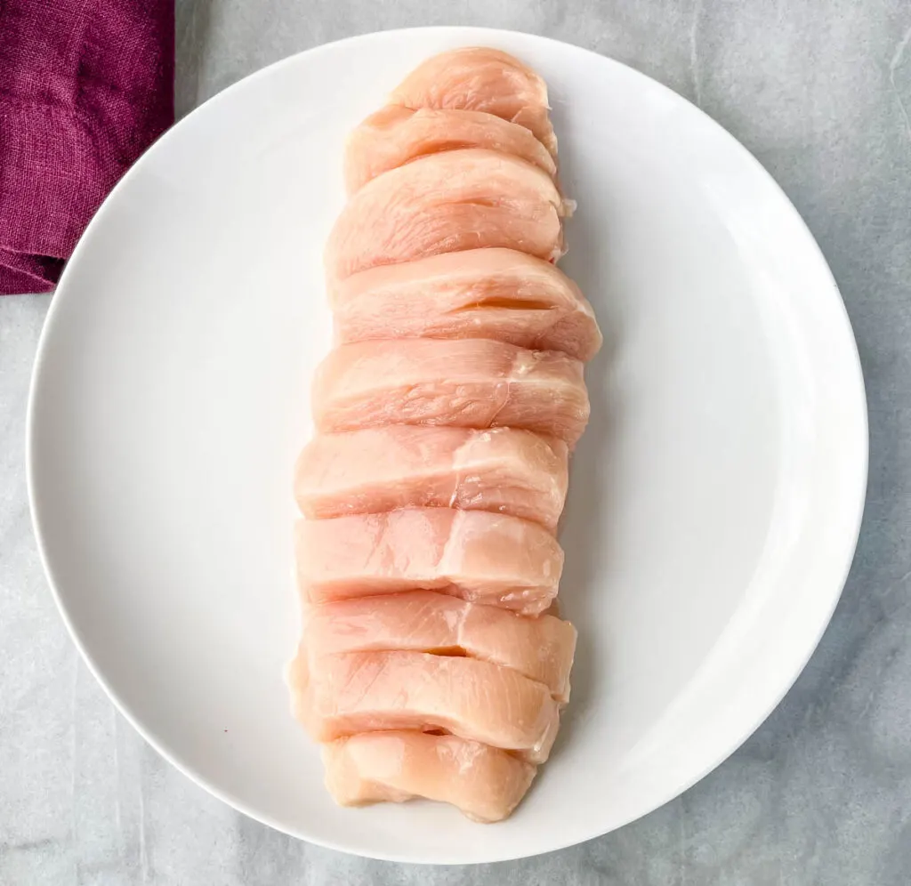 raw sliced chicken breast on a white plate