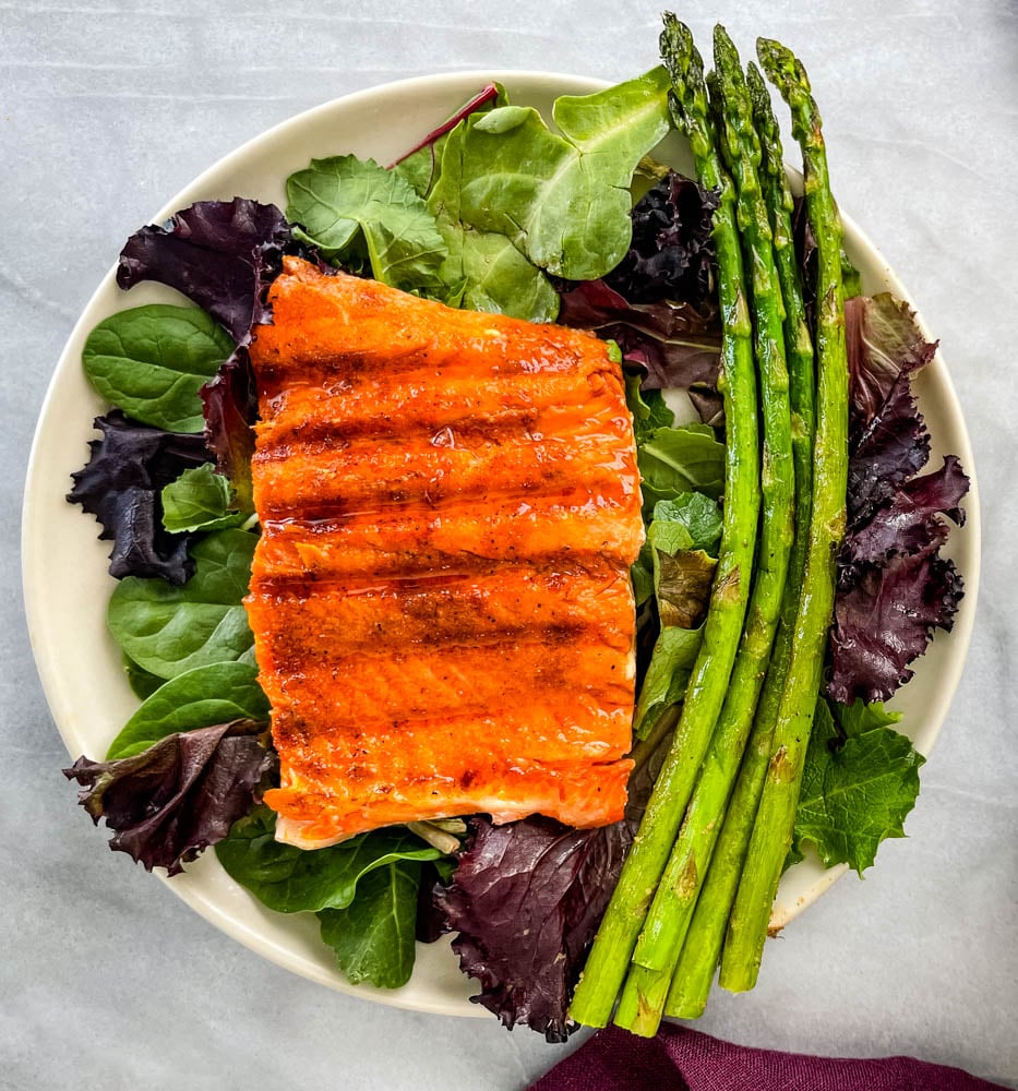 maple glazed salmon on a plate with asparagus and mixed greens