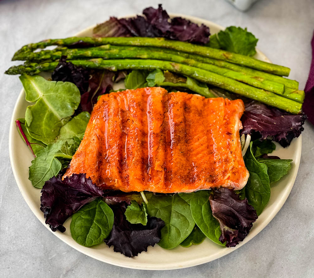 maple glazed salmon on a plate with asparagus and mixed greens