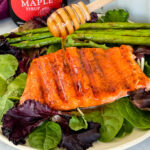 maple glazed salmon drizzled in syrup on a plate with asparagus and mixed greens