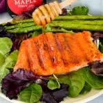 maple glazed salmon drizzled in syrup on a plate with asparagus and mixed greens