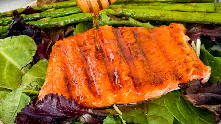 maple glazed salmon drizzled in syrup on a plate with asparagus and mixed greens