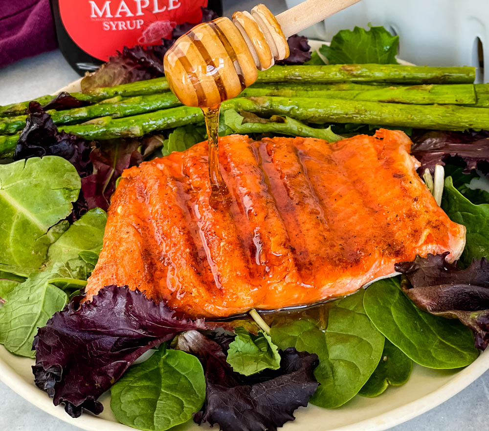 maple glazed salmon drizzled in syrup on a plate with asparagus and mixed greens