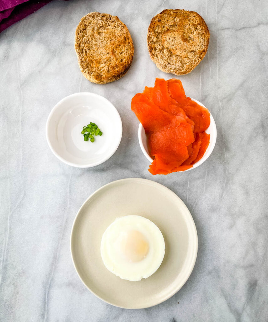 toasted English muffin, smoked salmon, green onions, and poached egg on a flat surface