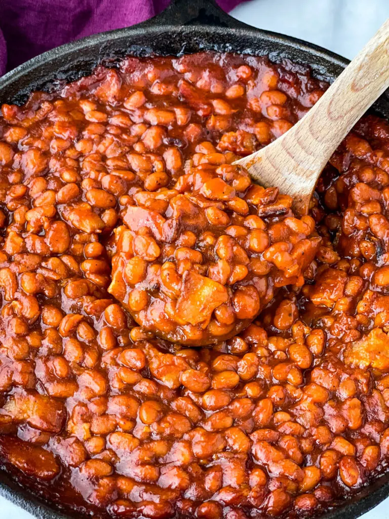 a wooden spoonful of Southern baked beans in a cast iron skillet