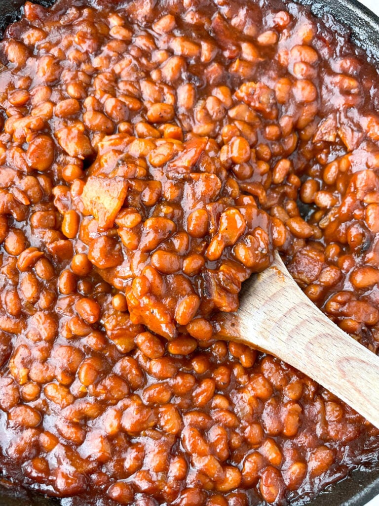 a wooden spoonful of Southern baked beans in a cast iron skillet